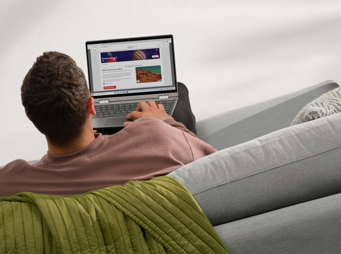 Osoba uczy się na laptopie na szarej kanapie.